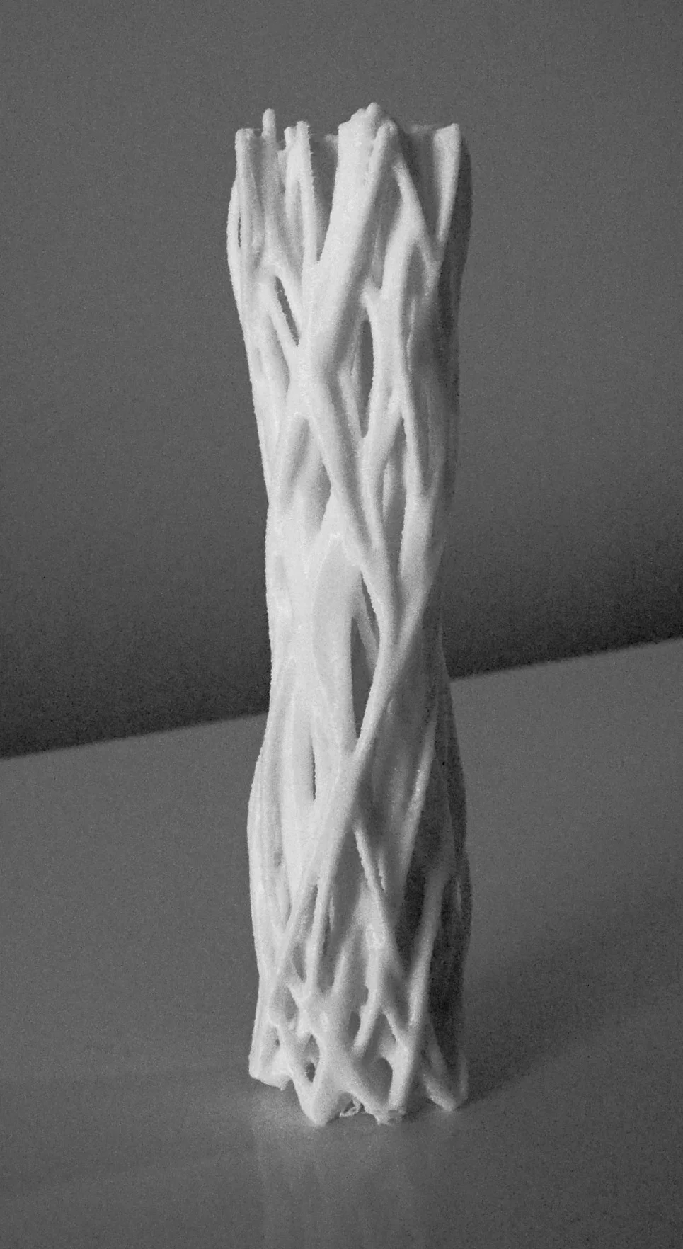 A tall cylindrical sculpture made of intertwined woven strands, shown in black and white against a plain background, suggesting layered time and continuity