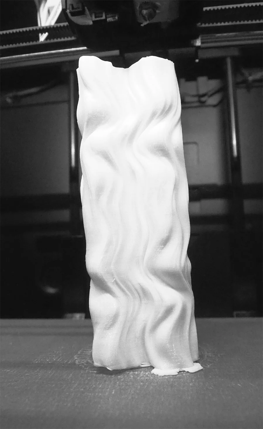 Tall white sculptural column with flowing wave-like ridges photographed against a plain backdrop